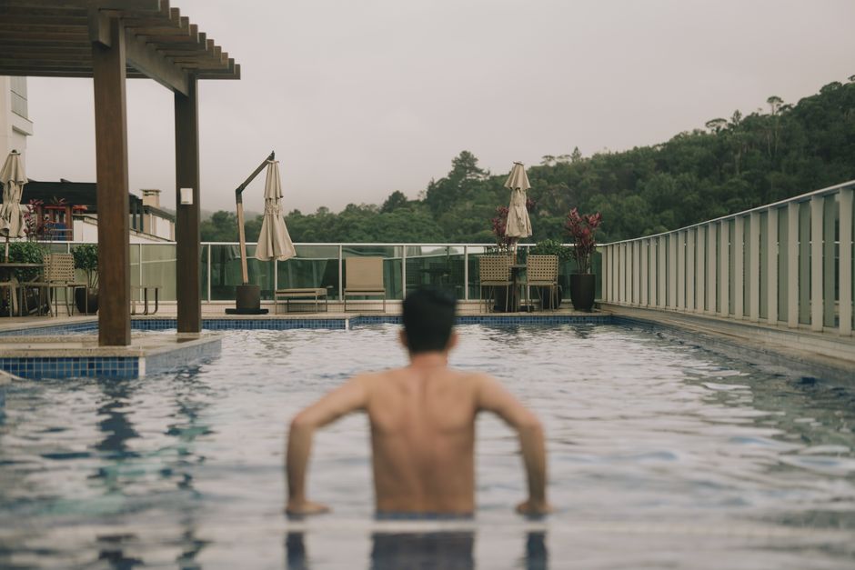 A man enjoys a refreshing swim in a rooftop pool with scenic green views.