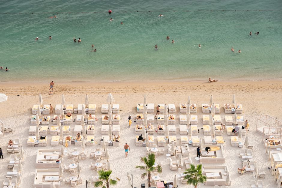 Aerial view of a luxurious beach resort with sun loungers and people enjoying the ocean.