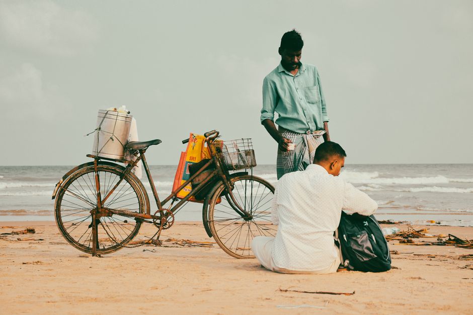Two men with a bicycle on a scenic beach during daytime, capturing a serene moment.
