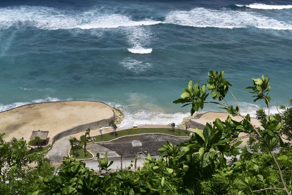 Aerial view of a tropical beach with lush greenery and turquoise ocean waves.