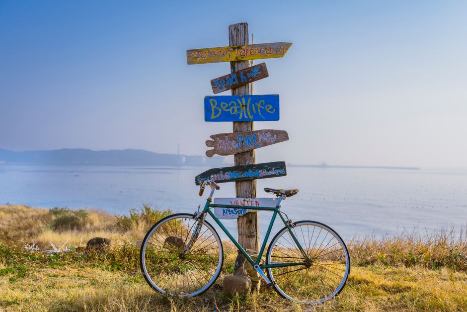 A lone bicycle rests against colorful directional signs overlooking a serene bay at dawn.