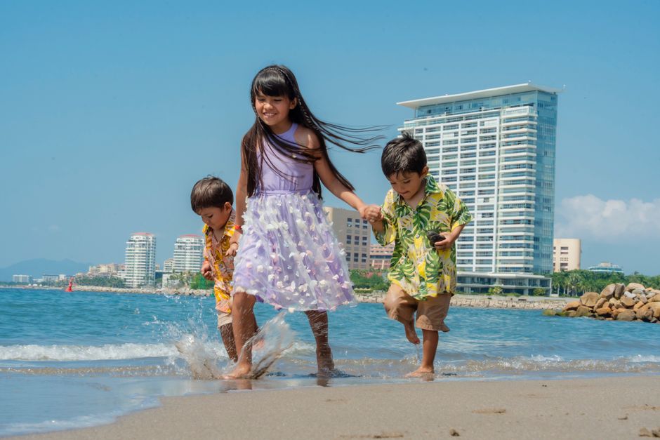Three children enjoying a sunny day at the beach, playing near the ocean waves.