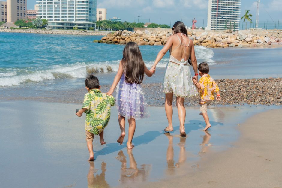 A family walks hand in hand on a sunny beach, enjoying a summer day.