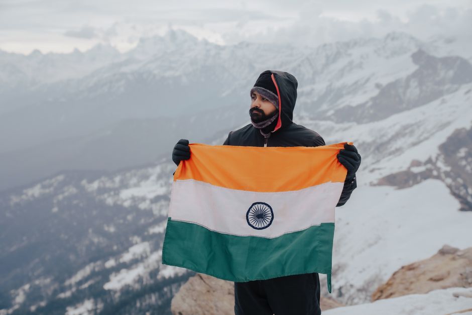 A man stands on a snowy mountain holding the Indian flag, showcasing patriotism and adventure.