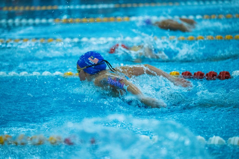 Swimmer performing butterfly stroke in a vibrant indoor pool during a race.