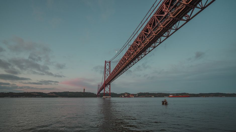 Beautiful view of a red bridge spanning a calm river at twilight, with soft pastel skies.
