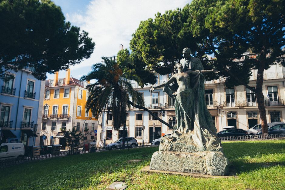 A vibrant city park scene featuring a historic monument amidst trees and colorful buildings.