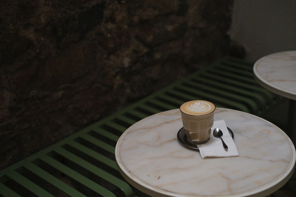 A beautifully crafted latte with delicate latte art sits on a marble table in a cozy café setting. The ambient lighting enhances the warm atmosphere.