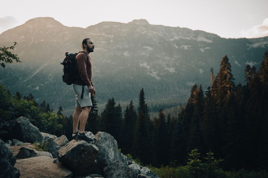 A man stands on rocky terrain, admiring the breathtaking mountain view at sunset, embodying adventure and exploration.