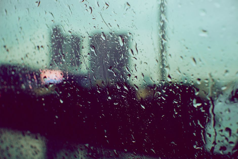 Raindrops on a window, with a blurred cityscape in the background, evoke a moody atmospher