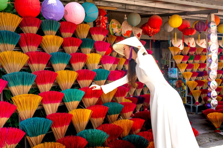 A woman in a traditional ao dai selects colorful incense sticks at an outdoor market