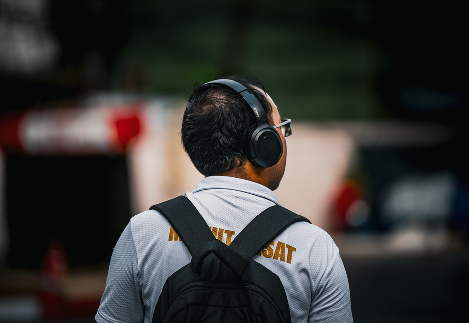 A person wearing headphones walks with a backpack in Bangkok's urban environment.