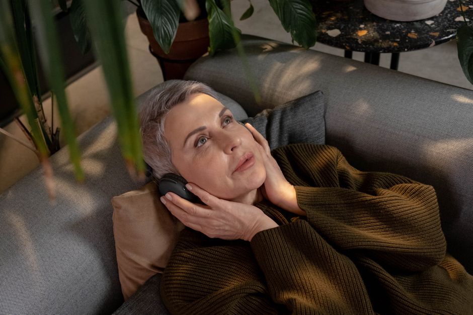 A senior woman with gray hair relaxing indoors, enjoying music on wireless headphones.