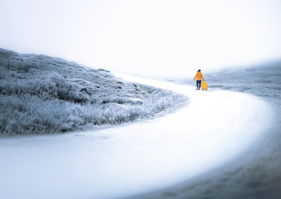 Person in a yellow coat walking on a snowy path with a suitcase, Norway.